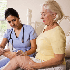 Home Care Assistant Bandaging Elderly Womans Leg